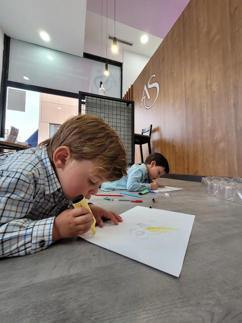 Dos niños dibujando tranquilamente en la sala de la clínica Ortodoncia Santonja, bajo el logotipo AS